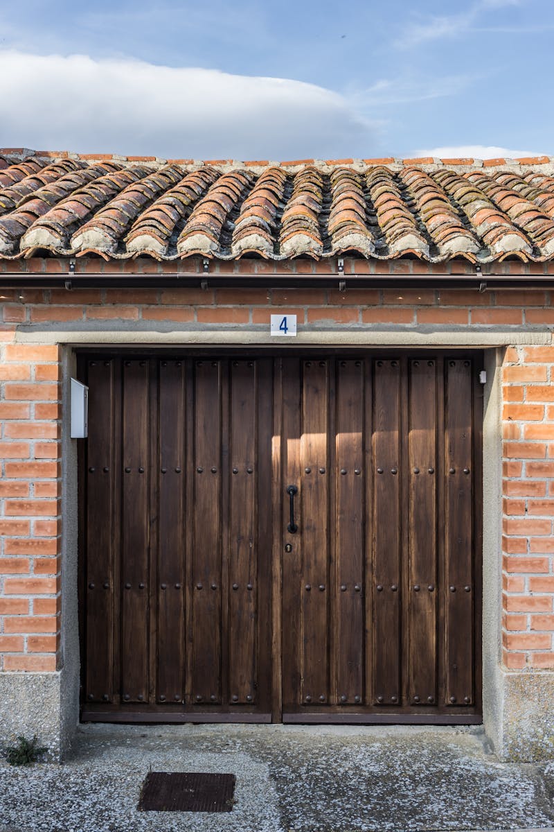 A rustic wooden door on a red brick house facade featuring a vintage tiled roof.
